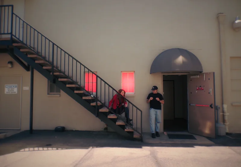 Still from Borrowed Time: a woman in a red jacket on a fire escape stair beside a man outside a stage door