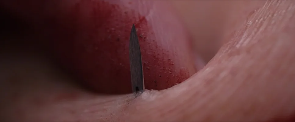 Frame from the SKIN ripomatic: a needle against skin in extreme close-up