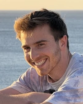 Teddy Hawke, smiling, with the ocean behind him at sunset